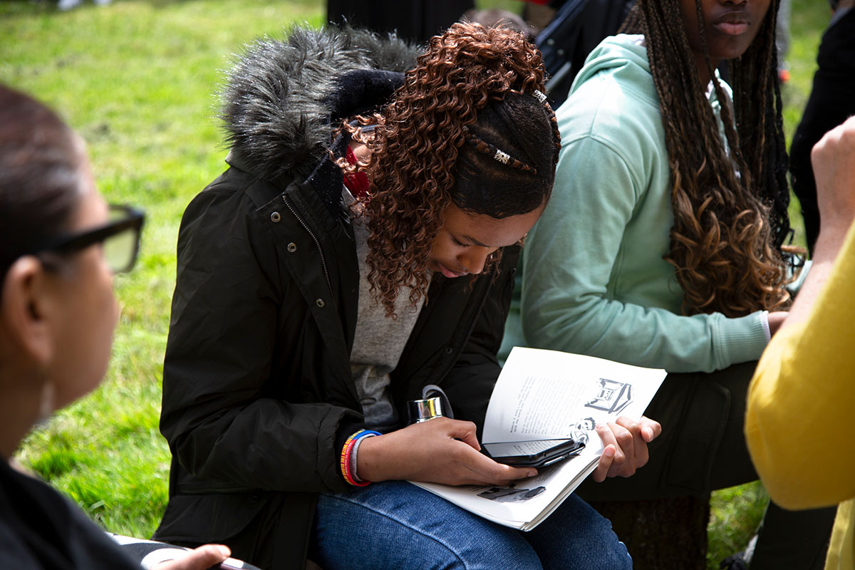 A young person is using her phone over an open book.